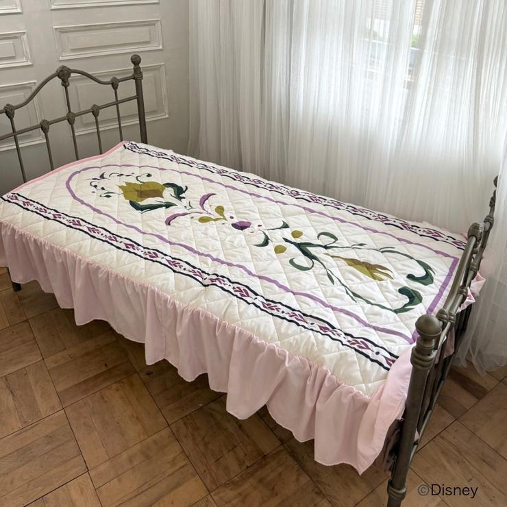 Single-size polyester 'Frozen' quilted pad with a pink ruffled edge displayed on a metal bed.