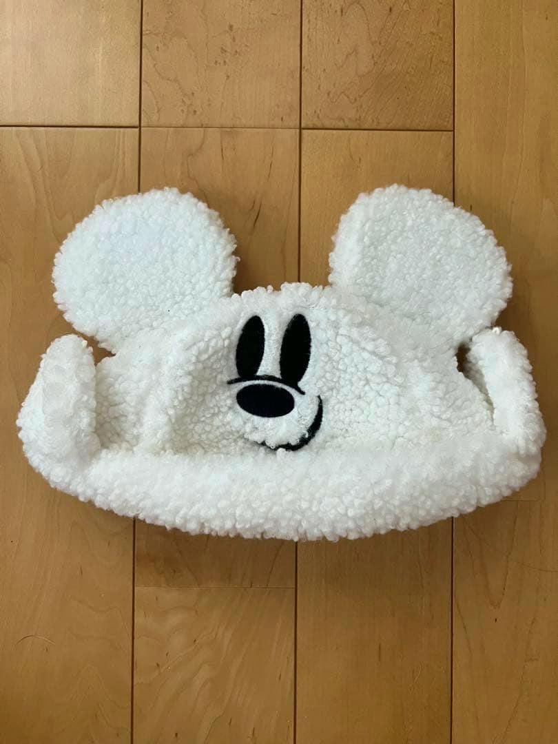 White fluffy Disney fan cap with rounded ears and an embroidered black face, shown flat on a wooden floor.
