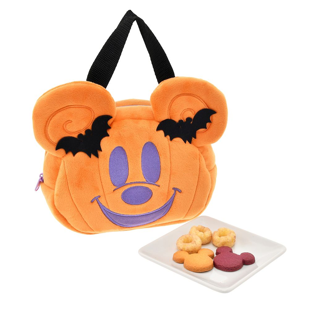 Orange Mickey-shaped Halloween plush bag with bat decorations shown beside a plate of assorted cookies.