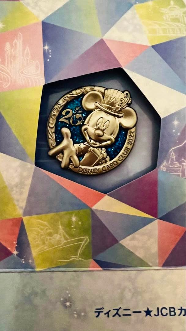Close-up photo of the Disney JCB 20th anniversary pin badge featuring Mickey Mouse in its colorful packaging.