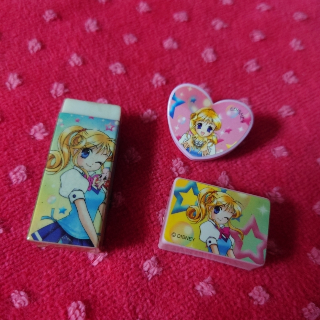 Three Disney Princess-themed erasers and a heart-shaped clip displayed on a pink textured background.