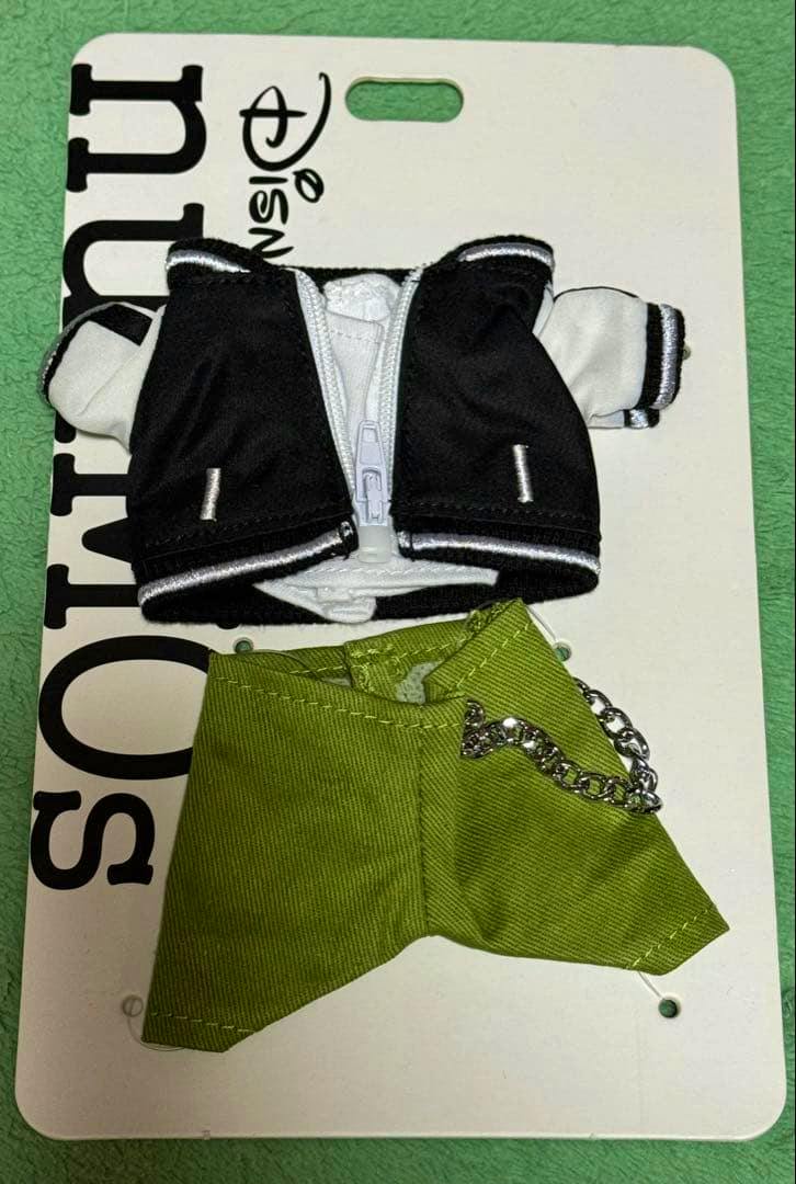 A black-and-white varsity-style jacket and a green fabric accessory for Disney nuiMOs dolls displayed on a white branded card.