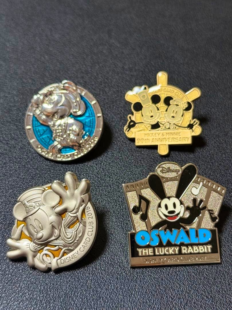 Four Disney pin badges from a JCB Card Club 4-piece set displayed on a dark textured background.