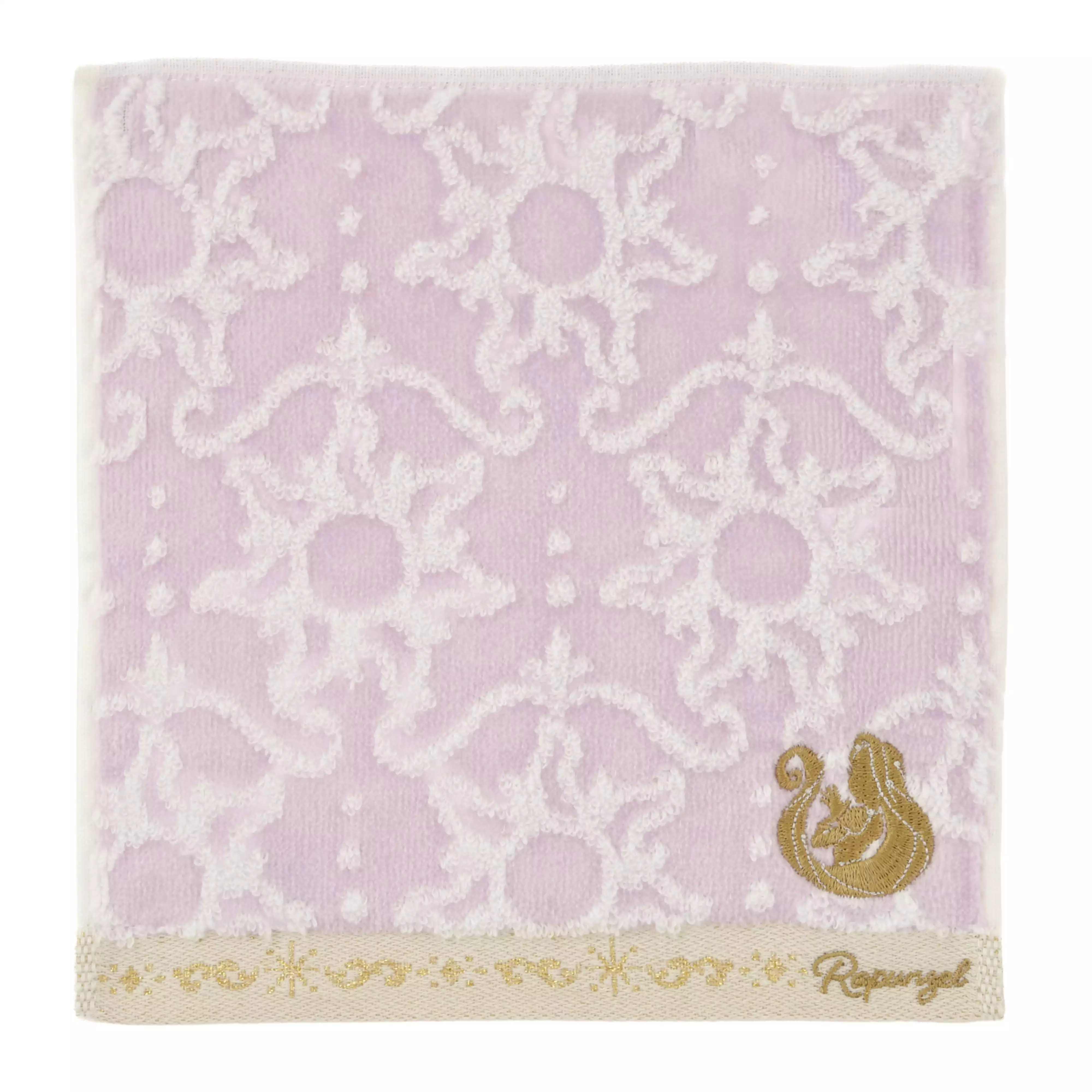 Square light purple cotton mini towel with a white decorative pattern and a small gold Rapunzel motif embroidered along the bottom edge.