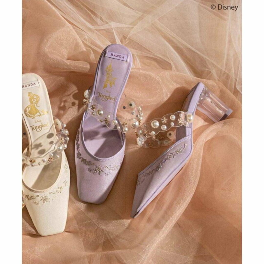 Purple sheer mule sandal with pearl-decorated clear strap and low clear block heel displayed alongside a white variant on a soft fabric backdrop.