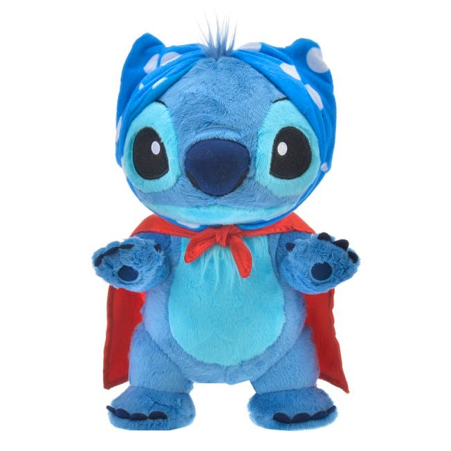 Front view of a blue Stitch plush wearing a red cape and blue polka-dot headband on a white background.