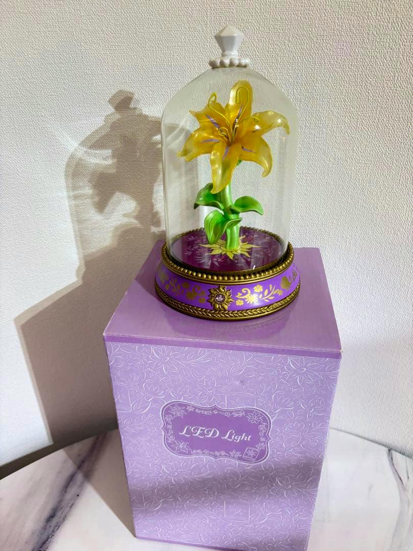 Photograph of the Rapunzel 10th anniversary magic flower LED light figure under a clear dome placed on its purple box.