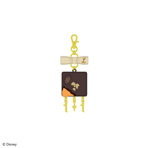 Illustration of the Lilia Vanrouge La Bonbonniere brooch charm showing a dark square charm with a beige bow and gold hardware.