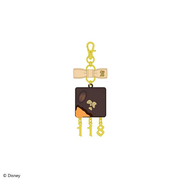 Illustration of the La Bonbonnière brooch charm for Malleus Draconia, a square chocolate‑themed charm with a bow and three small dangling gold charms.
