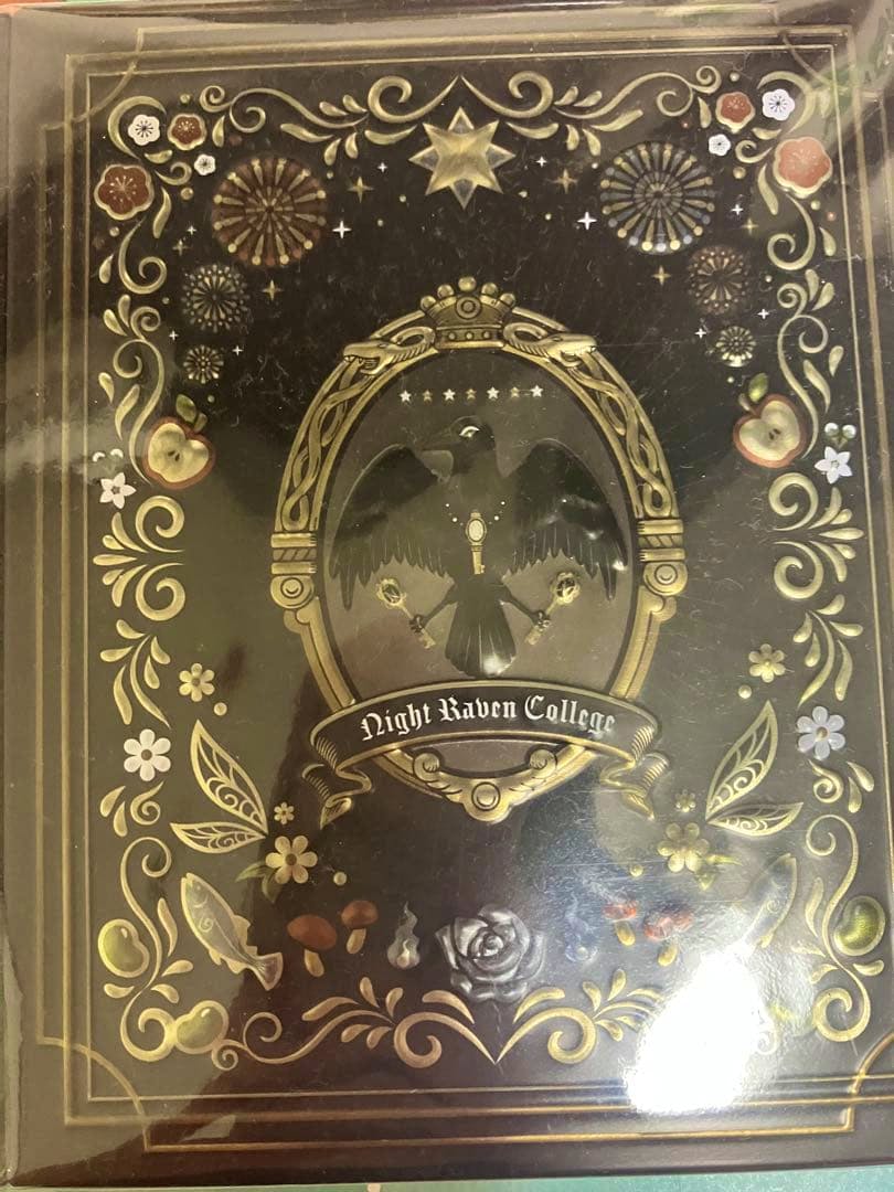 Front of the Twisted Wonderland baked chocolate tin showing a Night Raven College emblem and ornate gold decorative border.