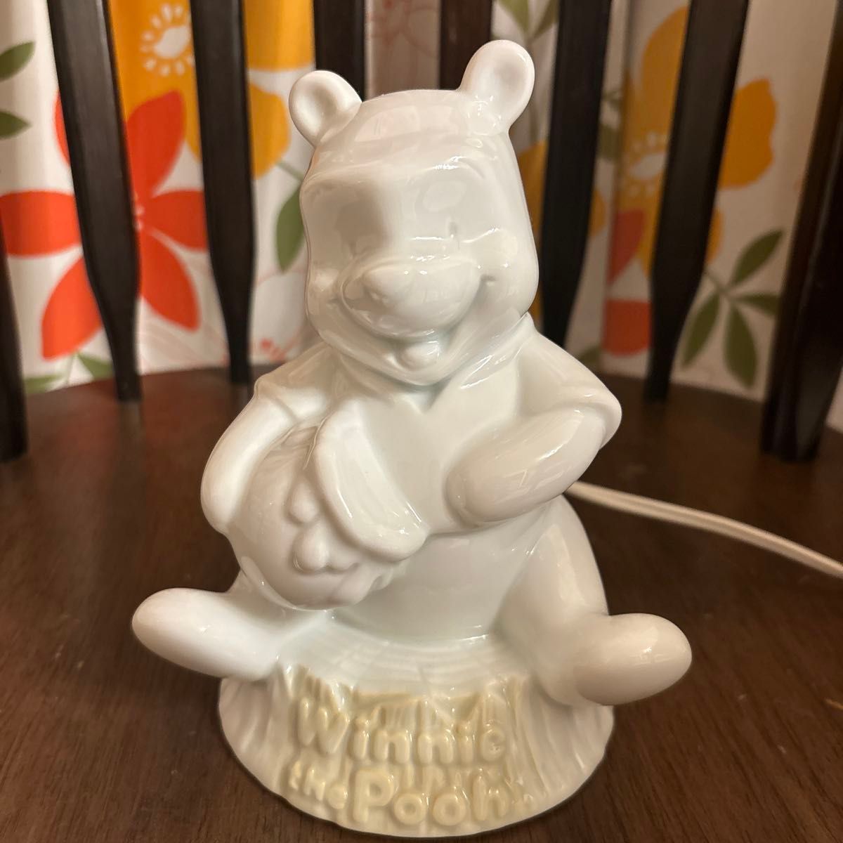 Front view of a white ceramic Winnie the Pooh figure lamp sitting on a wooden surface.