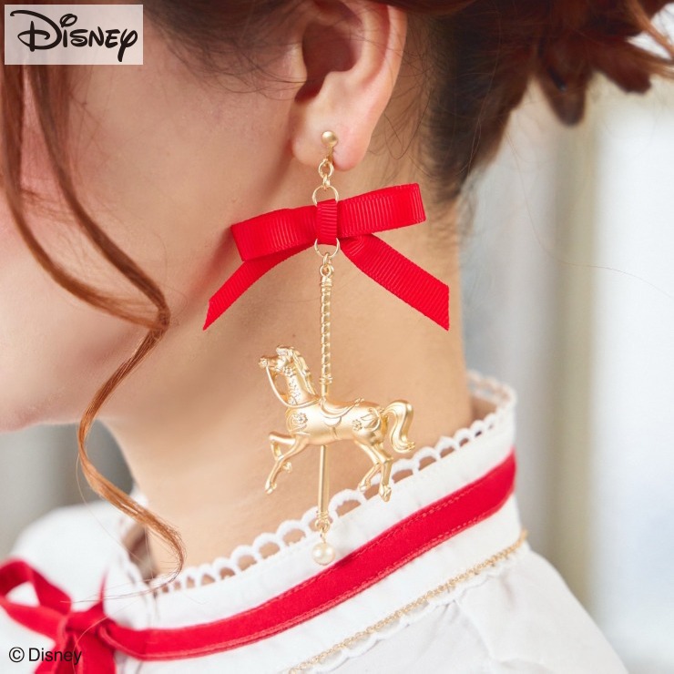 Side view of a woman's ear wearing a long Disney earring with a red ribbon and a gold carousel horse charm.