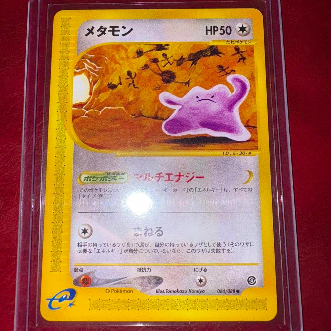 Front of a Japanese メタモン (Ditto) Pokémon trading card (064/088) in a clear sleeve on a red background.