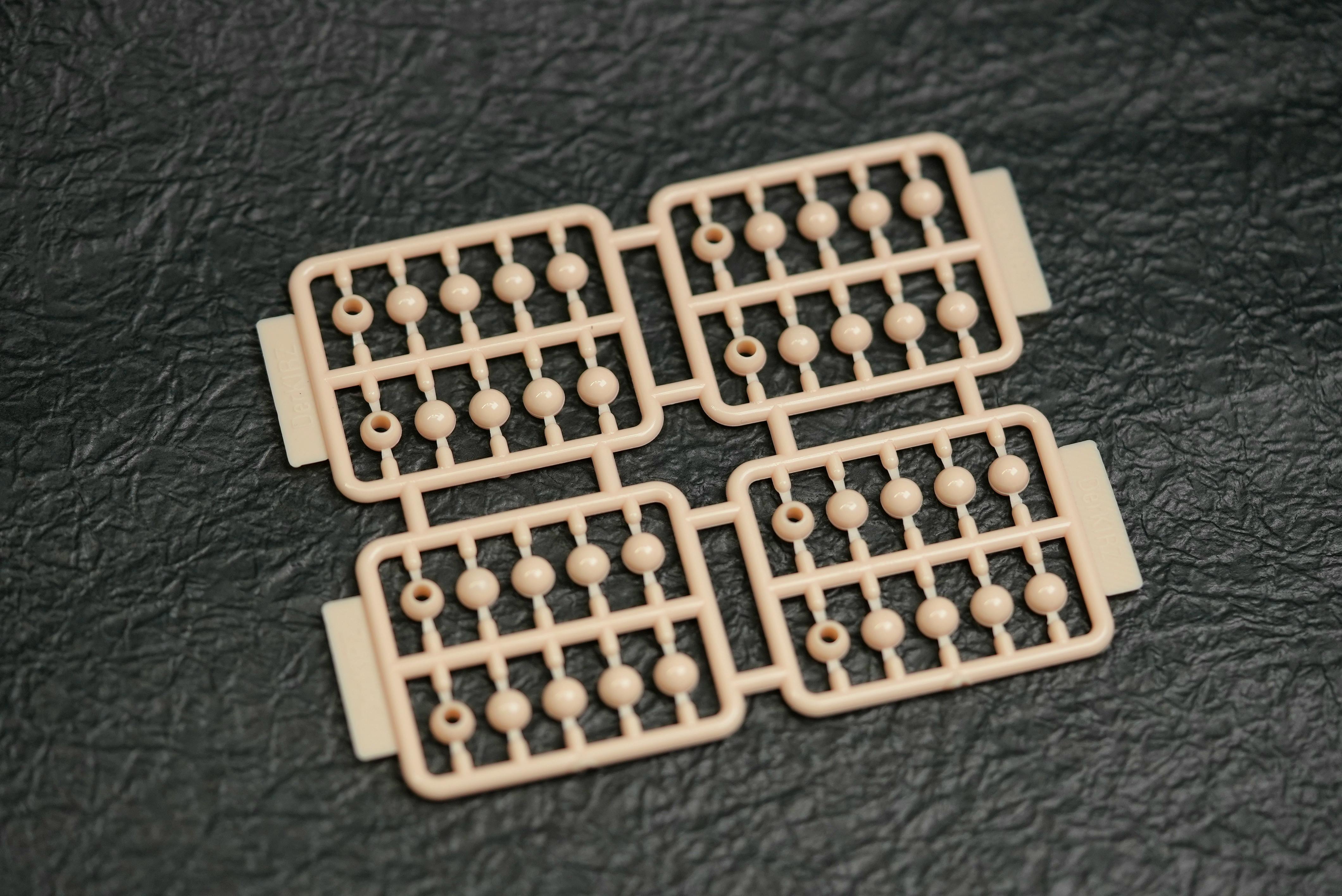 Beige plastic 1/12 head adapter sprues with small ball joints arranged on a black textured surface.