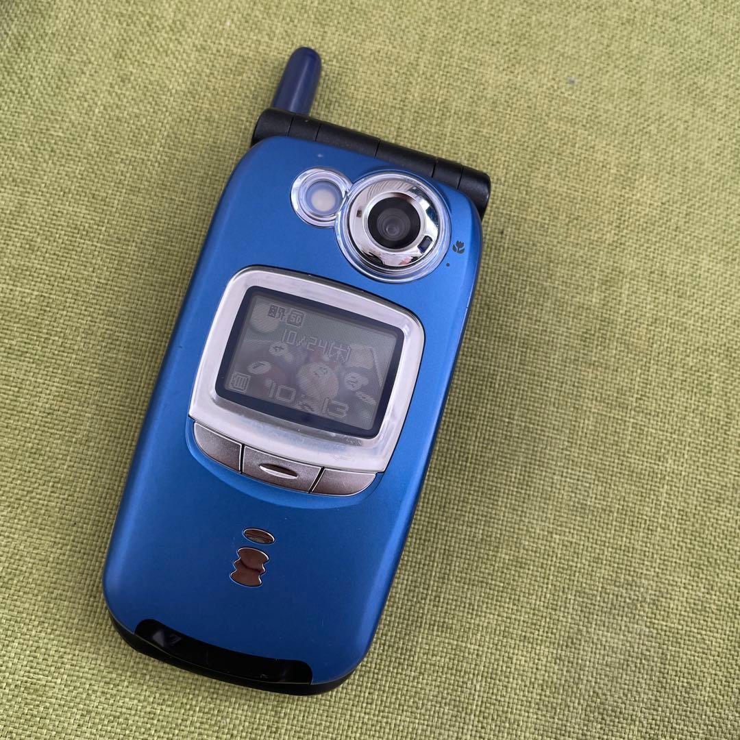 Closed blue docomo SH505I flip phone showing the external display, camera, and antenna on a green fabric surface.