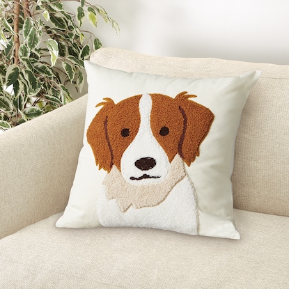 Square cushion cover with a brown-and-white dog face design displayed on a light-colored sofa.