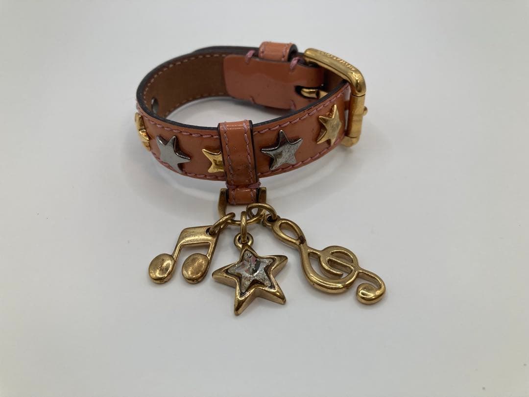 Brown cow leather bracelet with gold-tone star and musical-note charms laid on a white background.