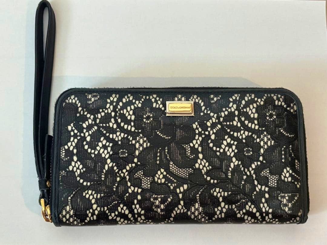 Black lace-pattern round-zip long wallet with a wrist strap and a small gold Dolce&Gabbana logo plate on the front.