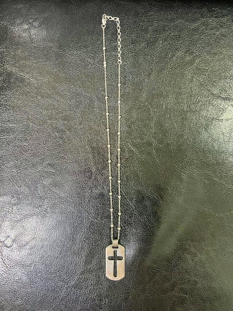 A Dolce & Gabbana necklace with a dog-tag style pendant featuring a cut-out cross laid flat on a black surface.