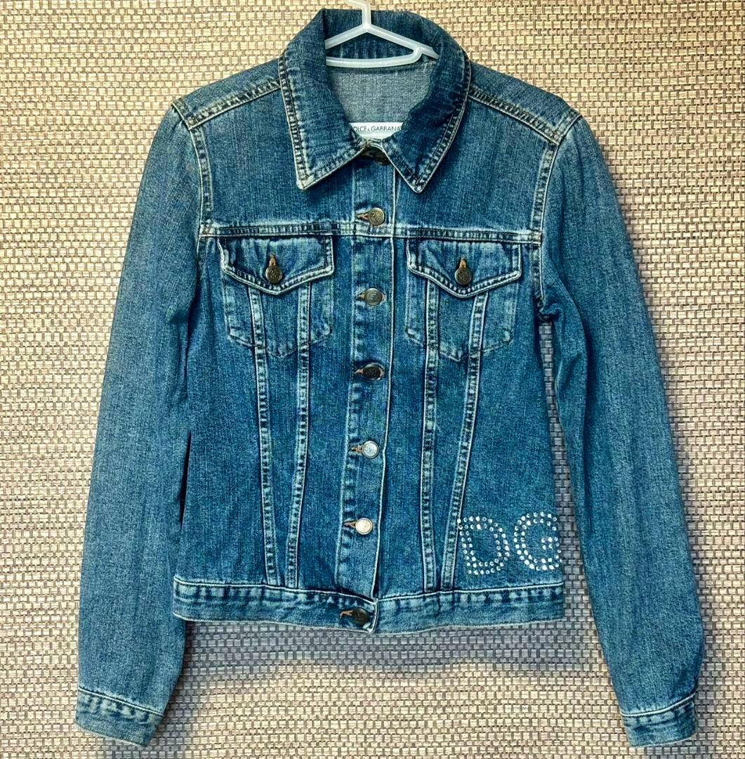 Front view of the Dolce & Gabbana men's denim jacket with long sleeves and rhinestone "DG" detail, hanging on a hanger.