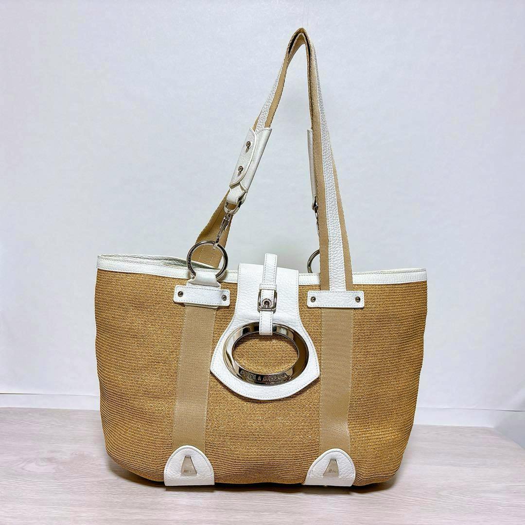 Front view of a Dolce & Gabbana straw tote bag with white leather trim and an oval metal logo.