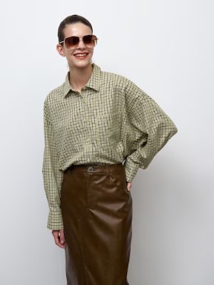 Model wearing a green checked dolman-sleeve women's shirt tucked into a brown skirt.