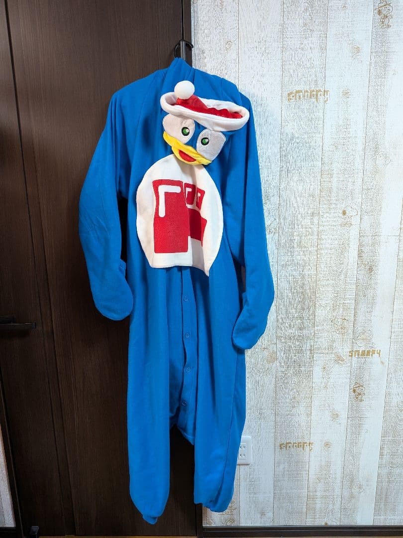 Front view of a blue Donpen kigurumi pajama with a character face hood and white-and-red chest patch hanging on a hook.