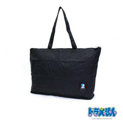 Black foldable tote bag with handles and a small Doraemon logo on the front photographed on a white background.