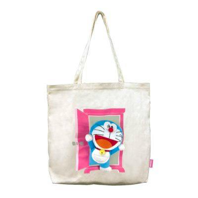 Cream-colored tote bag showing Doraemon emerging from a pink “Anywhere Door” print on the front.