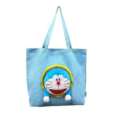 Light-blue polyester tote bag with a plush Doraemon face and yellow circular hoop on the front.