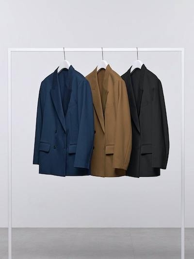 Three double-breasted oversized men's jackets in blue, brown, and black hanging on a clothing rack.