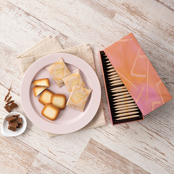 A box of individually wrapped cookies next to a plate with several cookies and chocolate pieces on a wooden surface.