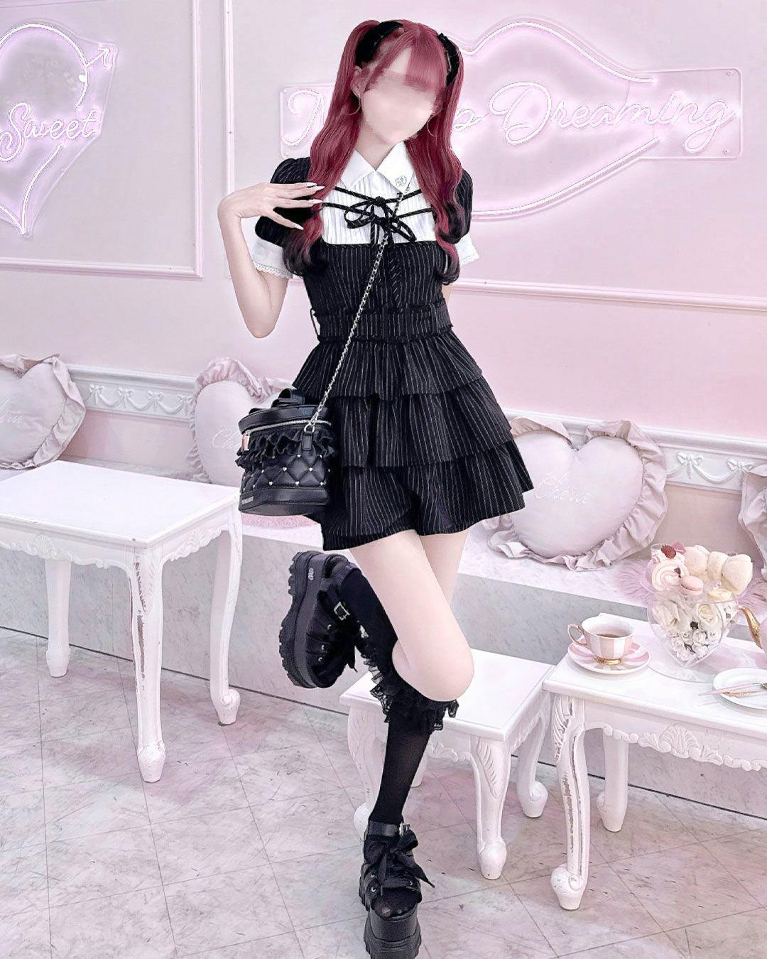 A model wearing the double ribbon tiered pants set-up in black standing full-length in a pink room.