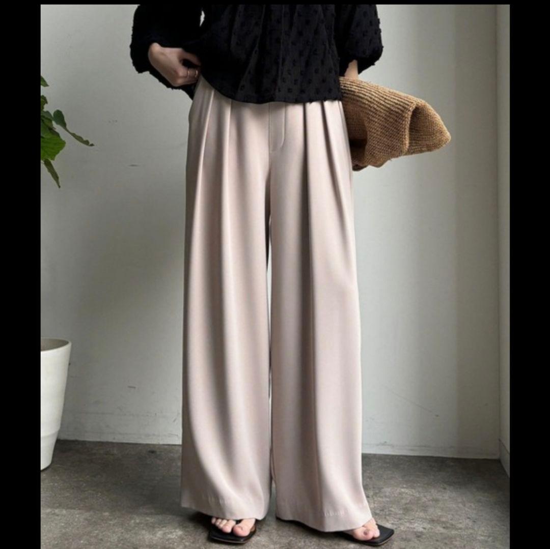Front view of the beige DouDou tuck wide women's pants worn by a model standing indoors.