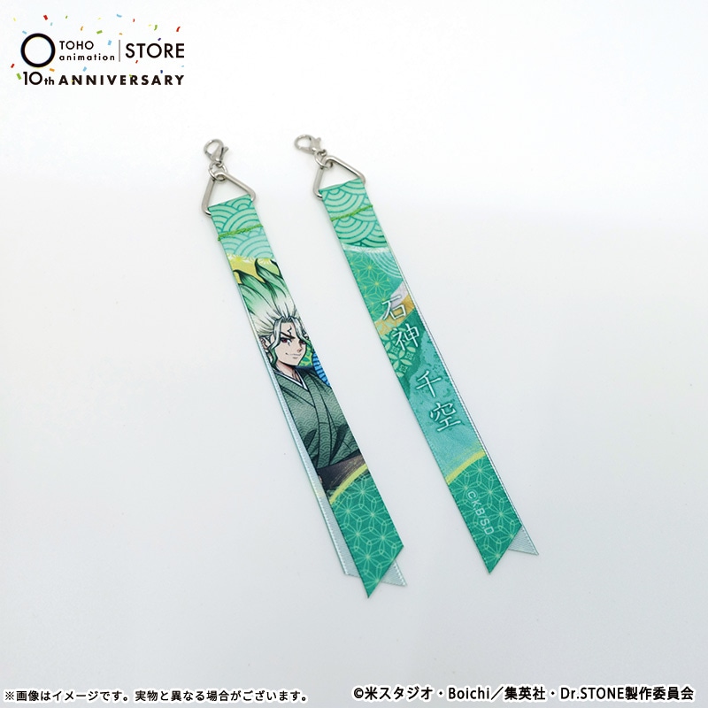 Photo of two fabric ribbon keychain charms (Dr.STONE 石神千空 TaS10th Ver.) showing front and back designs on a white background.