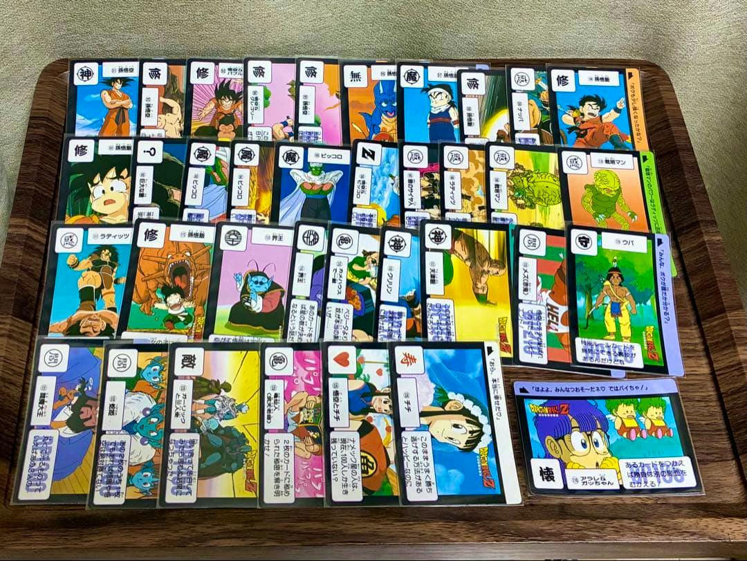Several Dragon Ball Carddass trading cards laid out in rows on a wooden tray.
