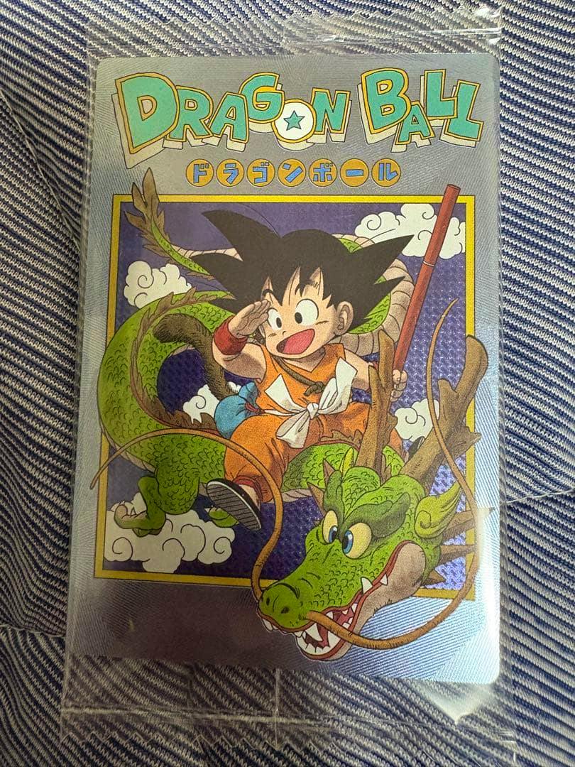Front of a Dragon Ball trading card showing young Son Goku with Shenron, sleeved and photographed on fabric.
