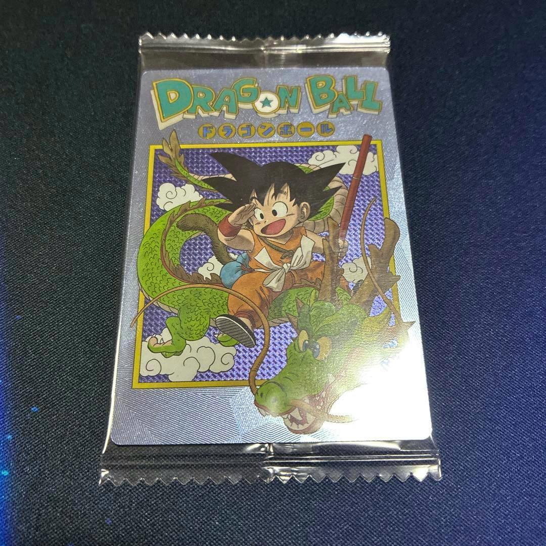 Sealed Dragon Ball trading card showing young Goku with Shenron on the front in its clear wrapper on a dark surface.
