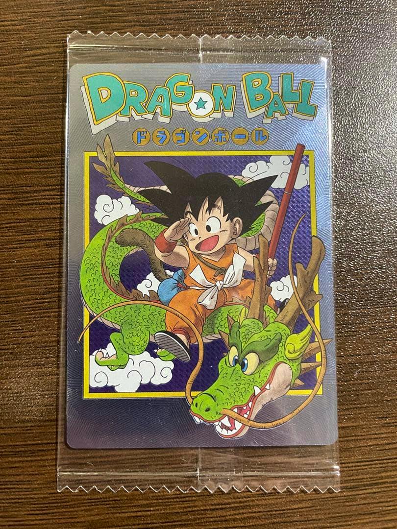 Front of a Dragon Ball trading card in a clear plastic sleeve showing Goku riding the dragon Shenron on a wooden surface.