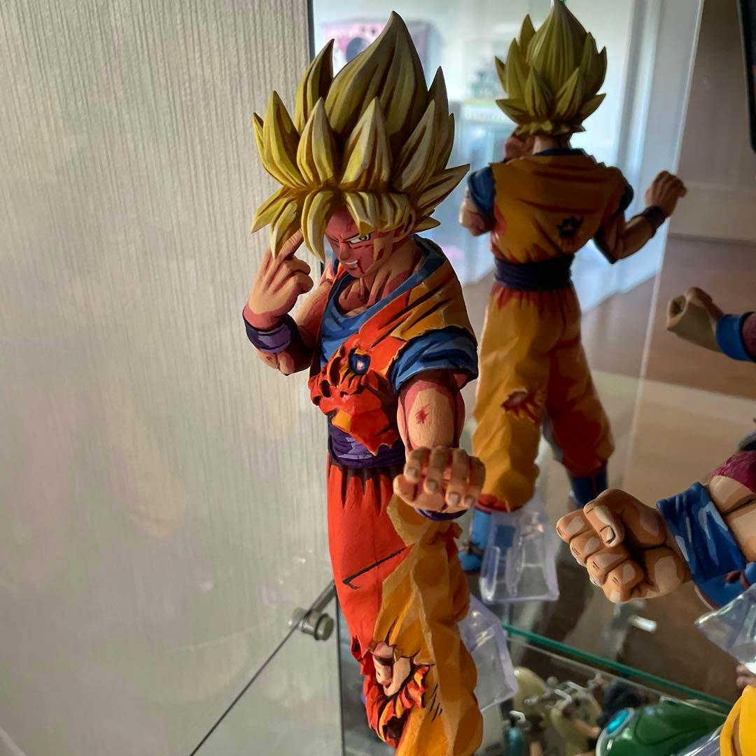Repainted Dragon Ball Son Goku figure with yellow hair and orange gi shown from the front with an outstretched hand on a display shelf.