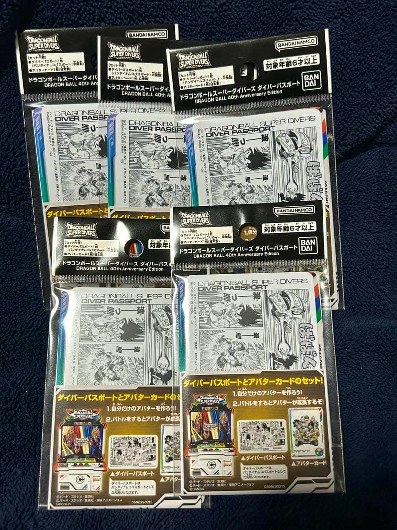 Photo showing five sealed Dragon Ball Super Divers Diver Passport 40th Anniversary Edition packages on a dark fabric background.