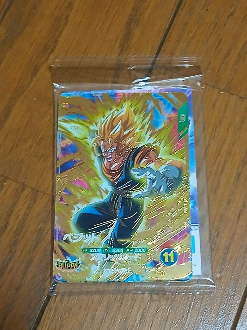 Front of an unopened Dragon Ball Super Divers BUPPA pack trading card in a clear plastic sleeve placed on a wooden floor.