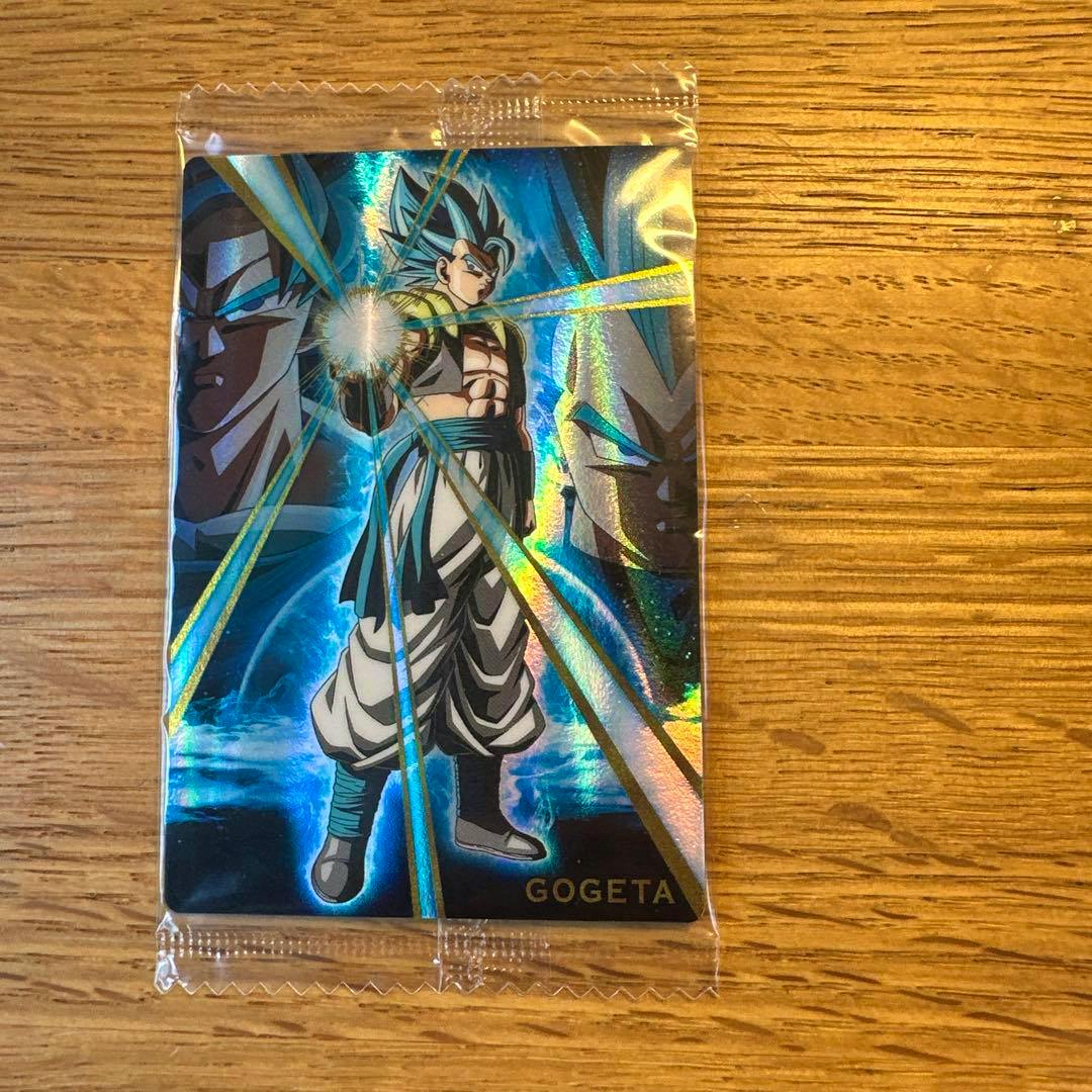 Holographic Dragon Ball photocard of Gogeta (GR) shown in a clear plastic sleeve on a wooden surface.