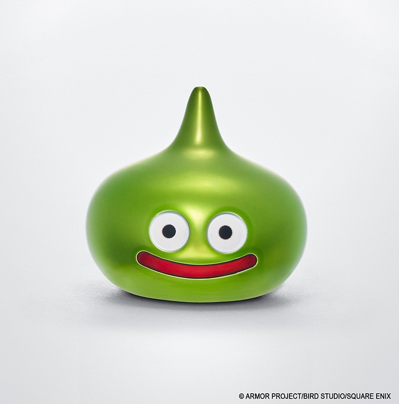 Metallic Lime Slime figure from Dragon Quest showing its face with round eyes and a red smiling mouth on a plain white background.