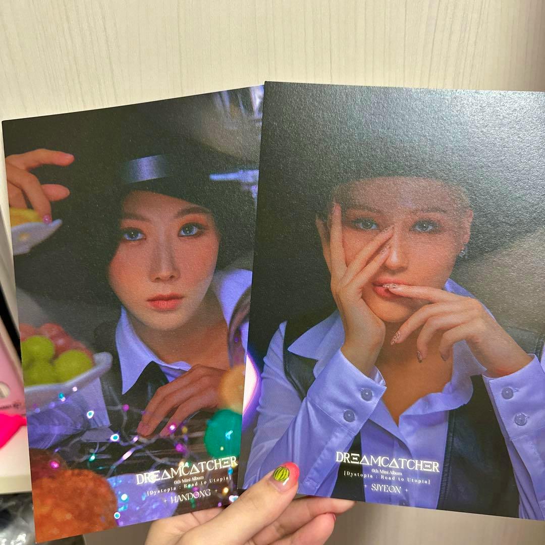 A hand holds two Dreamcatcher photocard portraits placed side by side.