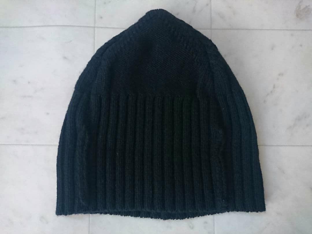 Black ribbed knit beanie laid flat on a light tile surface.