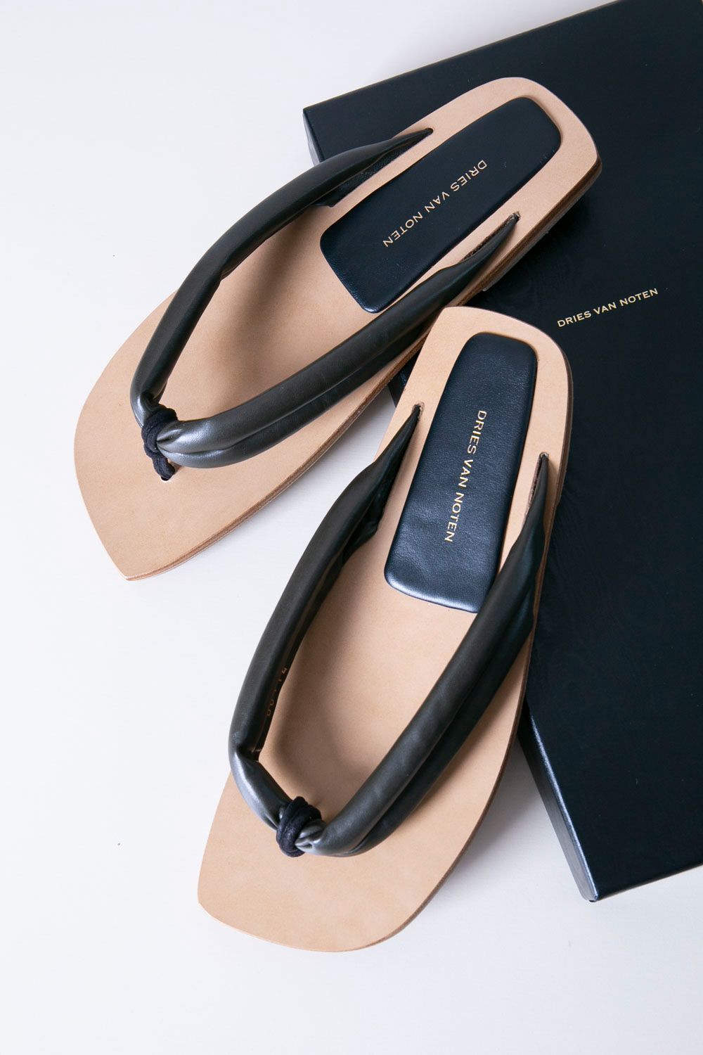 Top view of DRIES VAN NOTEN synthetic leather sandals with black padded straps on tan soles beside a black box.