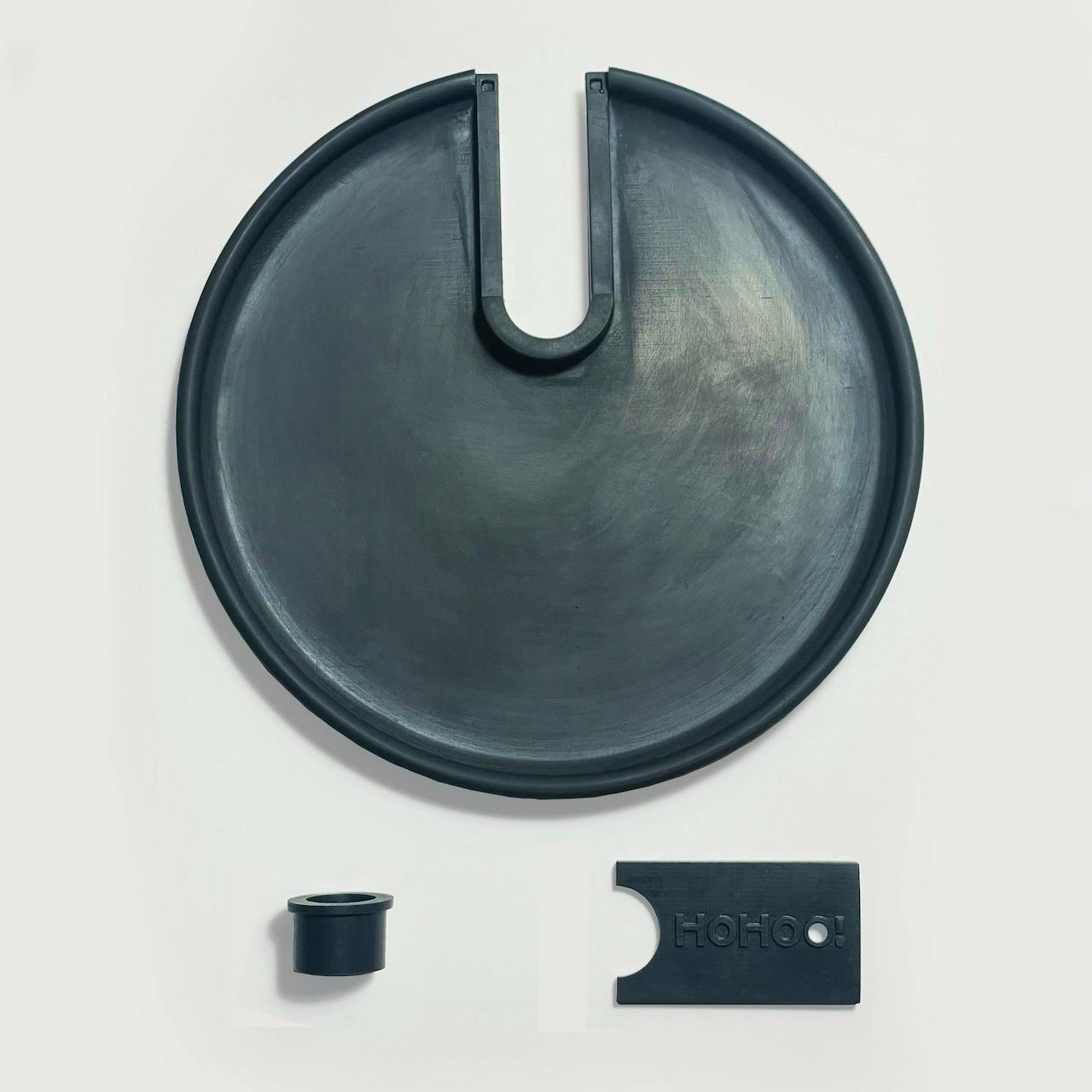 Three black plastic pieces of the product: a round tray with a U-shaped slot, a short cylindrical tube part, and a rectangular cap.