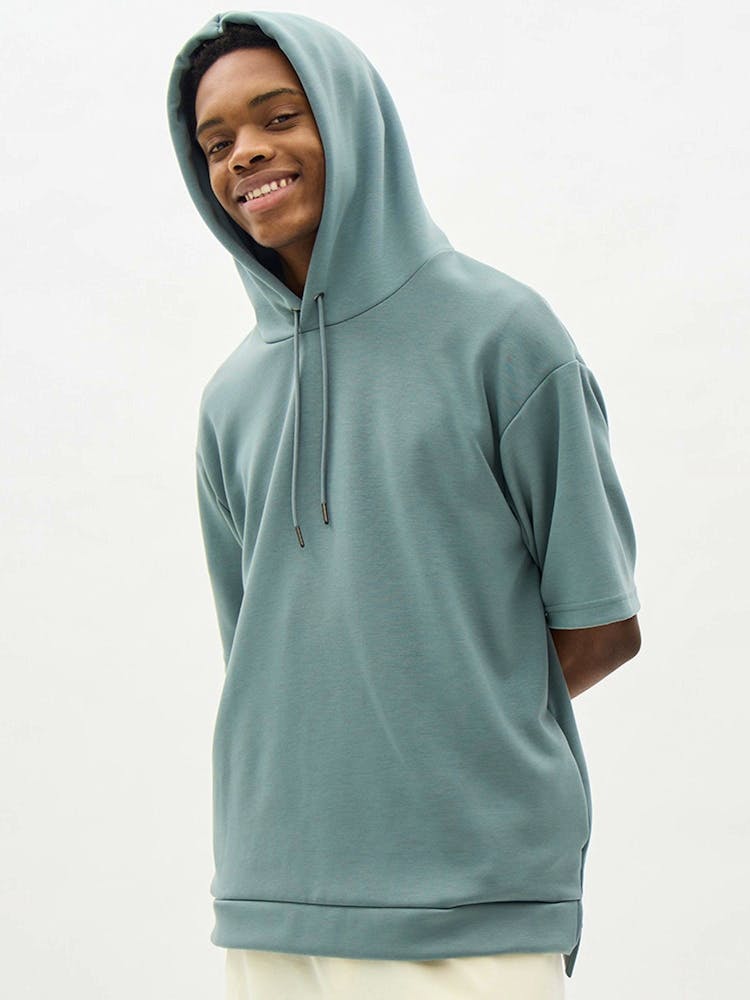 Model wearing a teal short-sleeve hooded parka shown from the front.