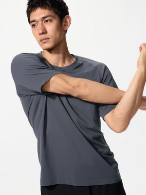 Male model wearing a gray short-sleeve T-shirt shown from the waist up while stretching his arms.